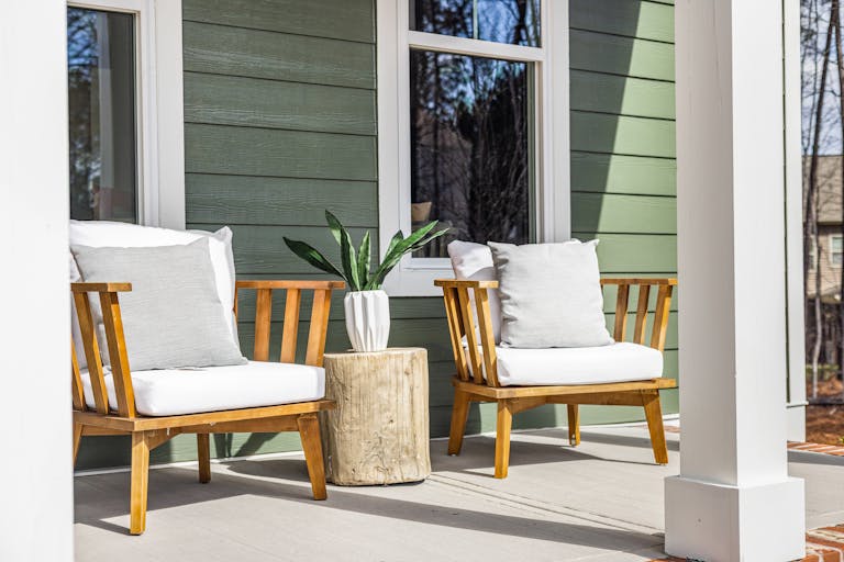 Charming porch featuring wooden armchairs, a rustic table, and a potted plant against green siding.
