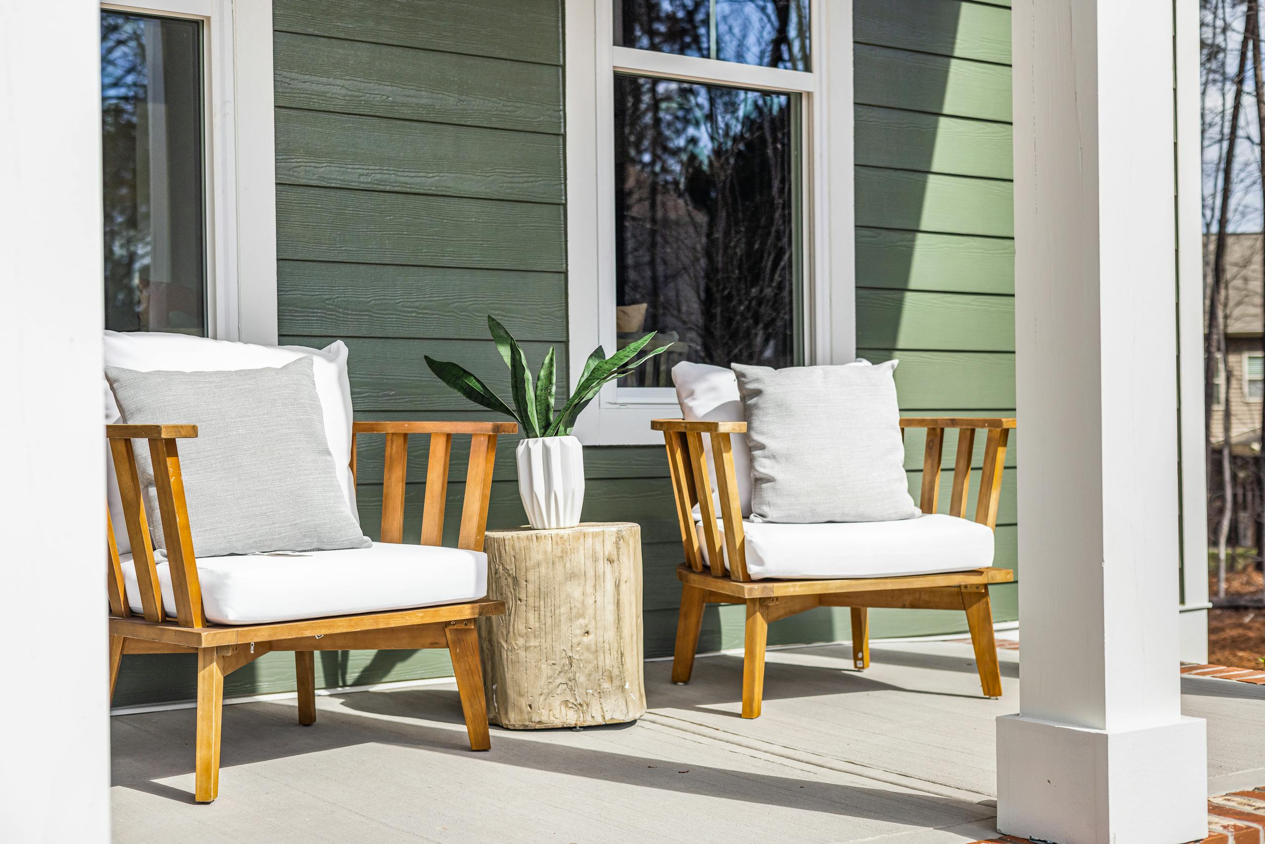 Charming porch featuring wooden armchairs, a rustic table, and a potted plant against green siding.