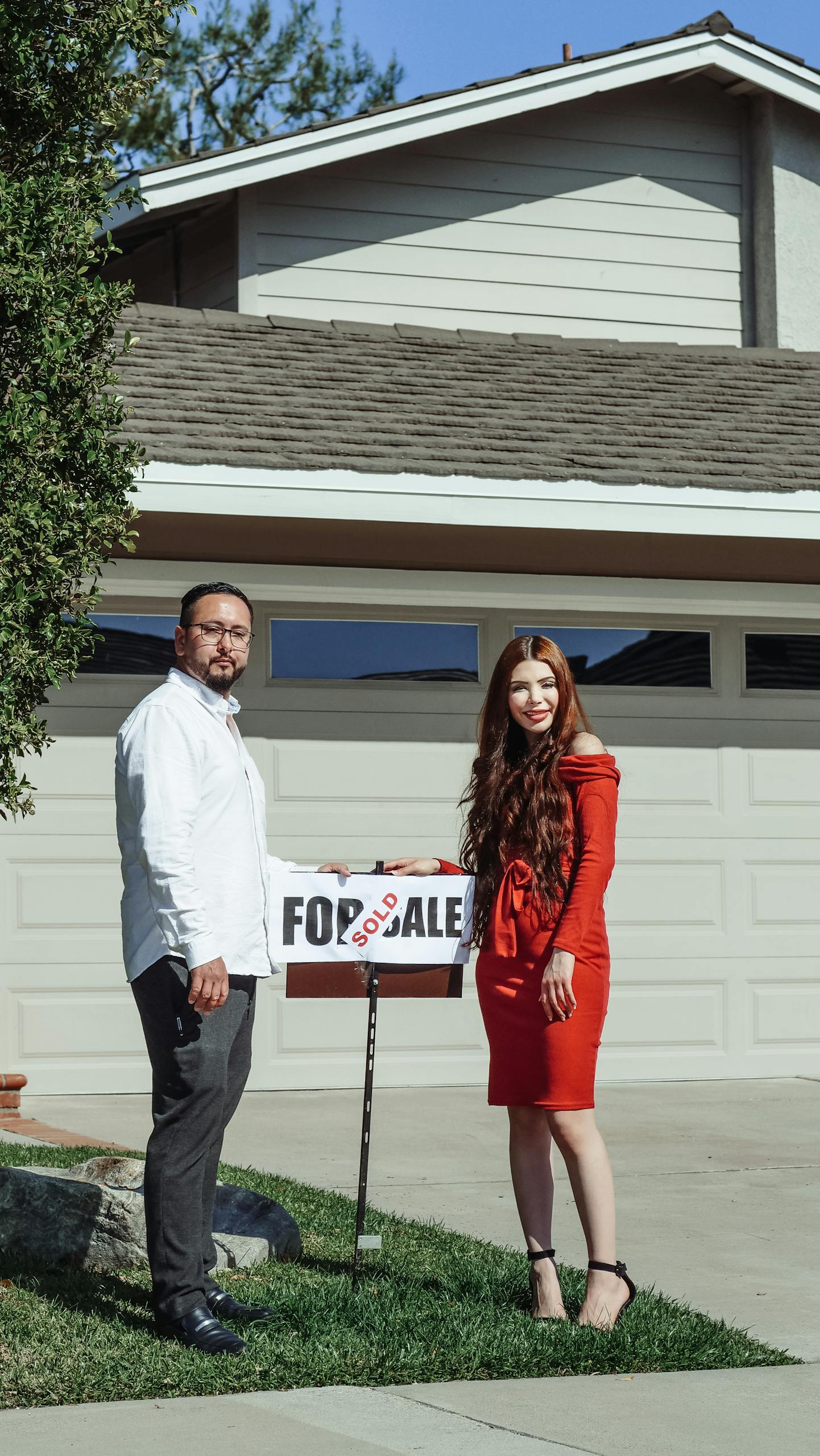Happy couple standing outside their newly purchased home with a sold sign in the front yard.